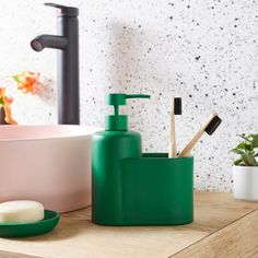 green soap dispenser and toothbrush holder on wooden table next to sink