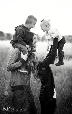 a man and woman are holding two small children in the middle of a grassy field