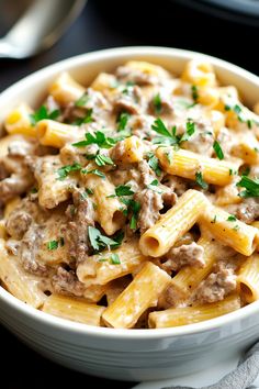 a white bowl filled with pasta covered in meat and sauce on top of a table