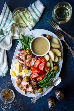 a white plate topped with meat and veggies next to a bowl of dressing