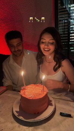 a man and woman sitting in front of a cake with lit candles