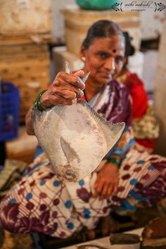 a woman sitting on the ground holding a fish in her hand and pointing at it