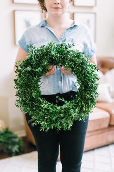 a woman holding a green wreath in front of her face while wearing black pants and a blue shirt