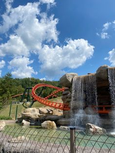 a water slide with a red roller coaster going over it's side in front of a cloudy blue sky