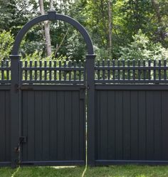 a black fence with an arch and gate in the center, surrounded by grass and trees