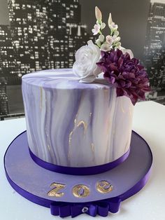 a purple and white marble cake with flowers on top, sitting on a table in front of a cityscape