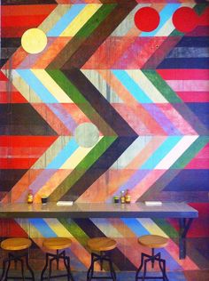 a colorful wall with three stools in front of it