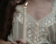 a woman holding a lit candle in her right hand and wearing a white dress with lace on it