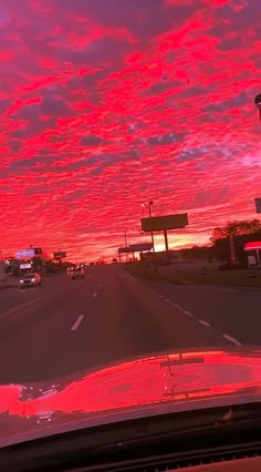 the sun is setting over an intersection with cars driving down it and red clouds in the sky