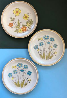 three plates with flowers painted on them sitting on a blue and green tablecloth next to each other