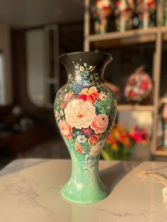 a vase with flowers painted on it sitting on a table in front of some shelves