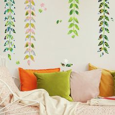 a white bed topped with lots of pillows next to a wall covered in colorful leaves