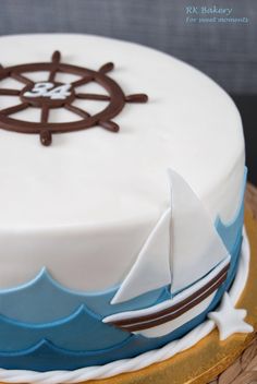 a white cake with blue icing and a brown boat on the top is sitting on a wooden platter