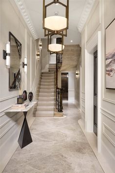 an elegant hallway with white walls and beige carpeted flooring, two chandeliers hanging from the ceiling