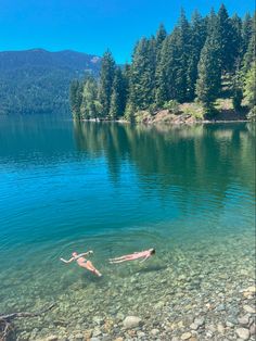 a person swimming in a lake surrounded by trees and rocks with the water crystal clear