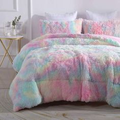 a bed with pink, blue and green comforter on it in a room next to a table