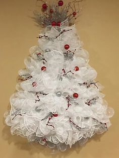 a white christmas tree with red and silver ornaments on it's top, hanging from a wall