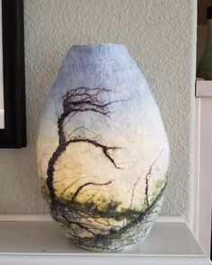 a vase with trees painted on it sitting on a shelf next to a framed photo