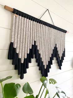 a wall hanging with black and white tassels next to a potted plant