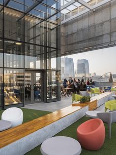 an outdoor seating area with chairs, tables and plants on the grass in front of large windows