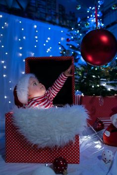 a baby dressed as santa claus is in a red and white box with christmas decorations around it