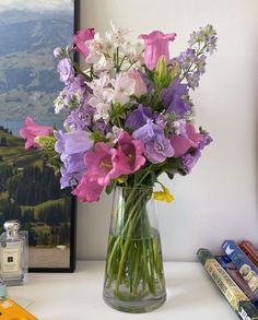 a vase filled with purple and white flowers on top of a table next to books