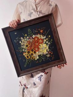 a woman holding up a framed painting with flowers on it