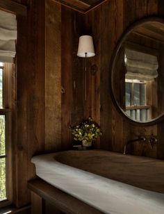 a bathroom with wood paneling and a round mirror on the wall next to a bathtub