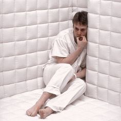 a man sitting on the floor in front of a white wall made out of mattresses