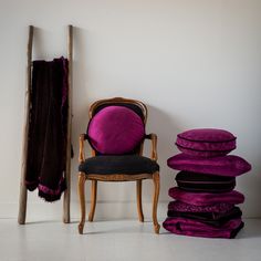 a purple chair sitting next to a pile of pillows and blankets on the floor in front of a white wall