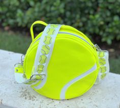 a tennis ball shaped purse sitting on top of a cement bench in front of bushes