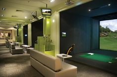 an indoor golf simulator with green and black walls, white couches, and chairs