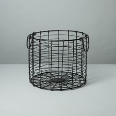 a black wire basket sitting on top of a white table next to a gray wall