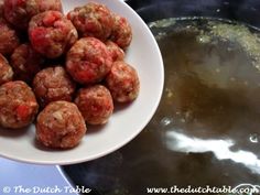 some meatballs are sitting on a white plate next to a pot of broth