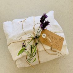 a wrapped gift with a tag and some lavenders on it is sitting on a white surface