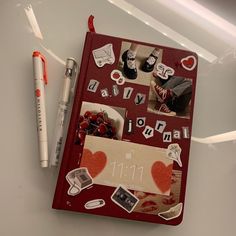 a red notebook covered in stickers and magnets next to a white pen on top of a table