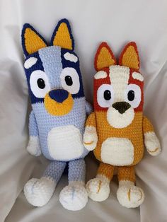 two crocheted stuffed animals sitting next to each other on a white sheet,