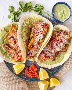 two fish tacos on a plate with guacamole and lime wedges