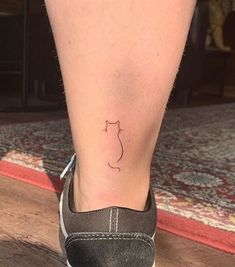 a small cat tattoo on the foot of a woman's right leg, which is sitting on top of a wooden floor