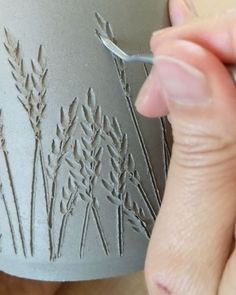 a person is painting a vase with flowers on the outside and grass on the inside