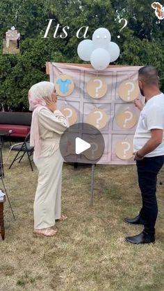 two people are standing in front of a sign with question marks on it and balloons