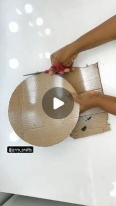 a person is cutting cardboard on top of a white surface with scissors and tape around the edges