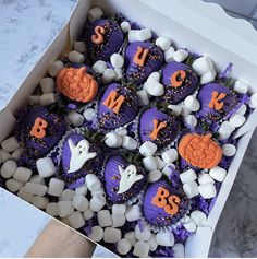 a box filled with purple and orange cupcakes covered in marshmallows