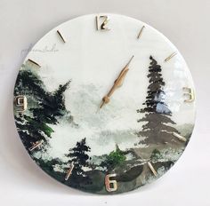 a white clock with trees painted on the face and numbers in gold, black and white