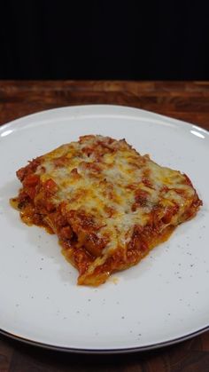 a piece of lasagna on a white plate sitting on top of a wooden table