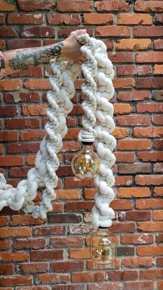 a person is hanging from a brick wall with yarn on it and a light bulb in the middle