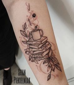 a tattoo on the arm of a person holding a coffee cup and stack of books