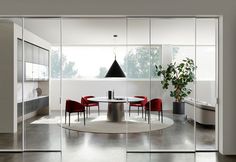 a round table surrounded by red chairs sits in the middle of a room with glass walls