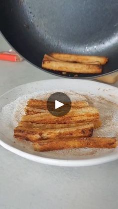 some french fries are on a white plate next to a frying pan and tongs