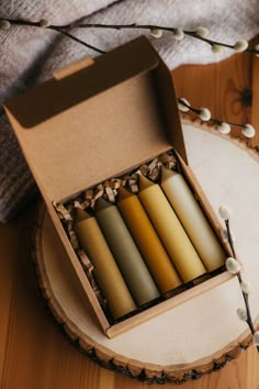 six candles in a box sitting on a wooden table next to a white and brown blanket